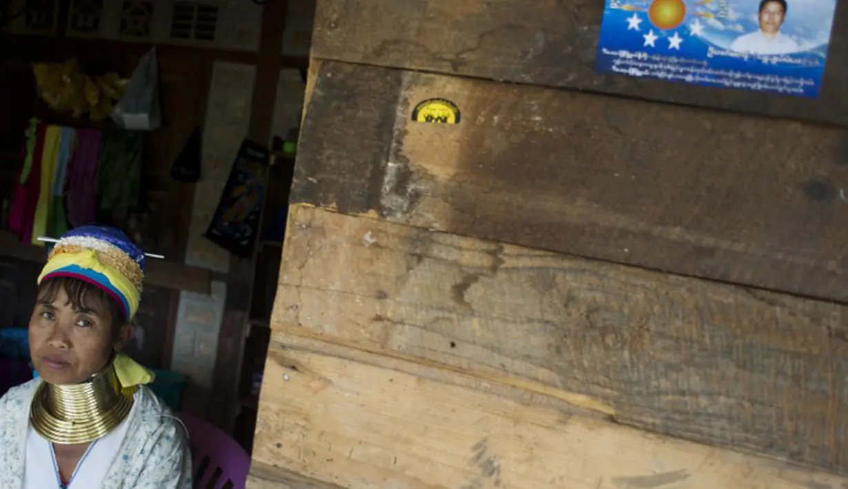 Wanita etnis Kayan duduk di dekat poster pemilu di desa PanPat, Kayan, Myanmar, Rabu (9/9/2015). Kaum perempuan Suku Kayan ini mengenakan banyak kalung berbentuk cincin di lehernya hingga membuat leher mereka panjang. (AFP PHOTO/Ye Aung THU)