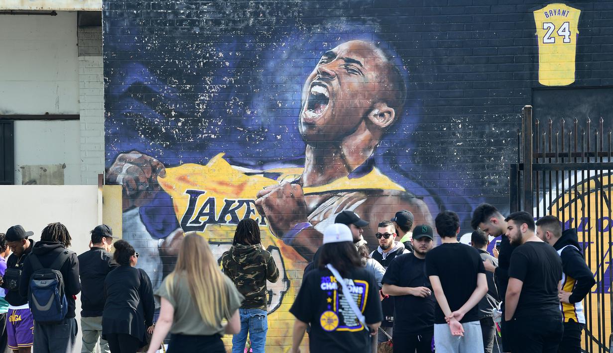 Sejumlah warga berkumpul untuk mengenang wafatnya Kobe Bryant di Staples Center, Los Angeles, Minggu (26/1). Akibat kecelakaan helikopter, legenda NBA itu wafat bersama sang putri. (AFP/Apu Gomes)