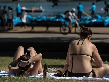 Dua wanita saat berjemur saat suhu musim panas mencapai sekitar 28 derajat di dekat Serpentine di Hyde Park di London, Inggris (5/7). (AFP Photo/Chris J Ratcliffe)