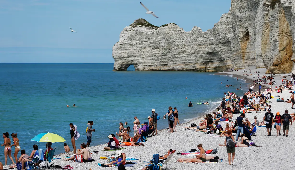 Wisatawan berjemur di pantai di Etretat, Prancis barat laut (17/7). Tebing-tebing dan pantai di Étretat menarik para seniman seperti Eugène Boudin, Gustave Courbet dan Claude Monet. (AFP Photo/Charly Triballeau)