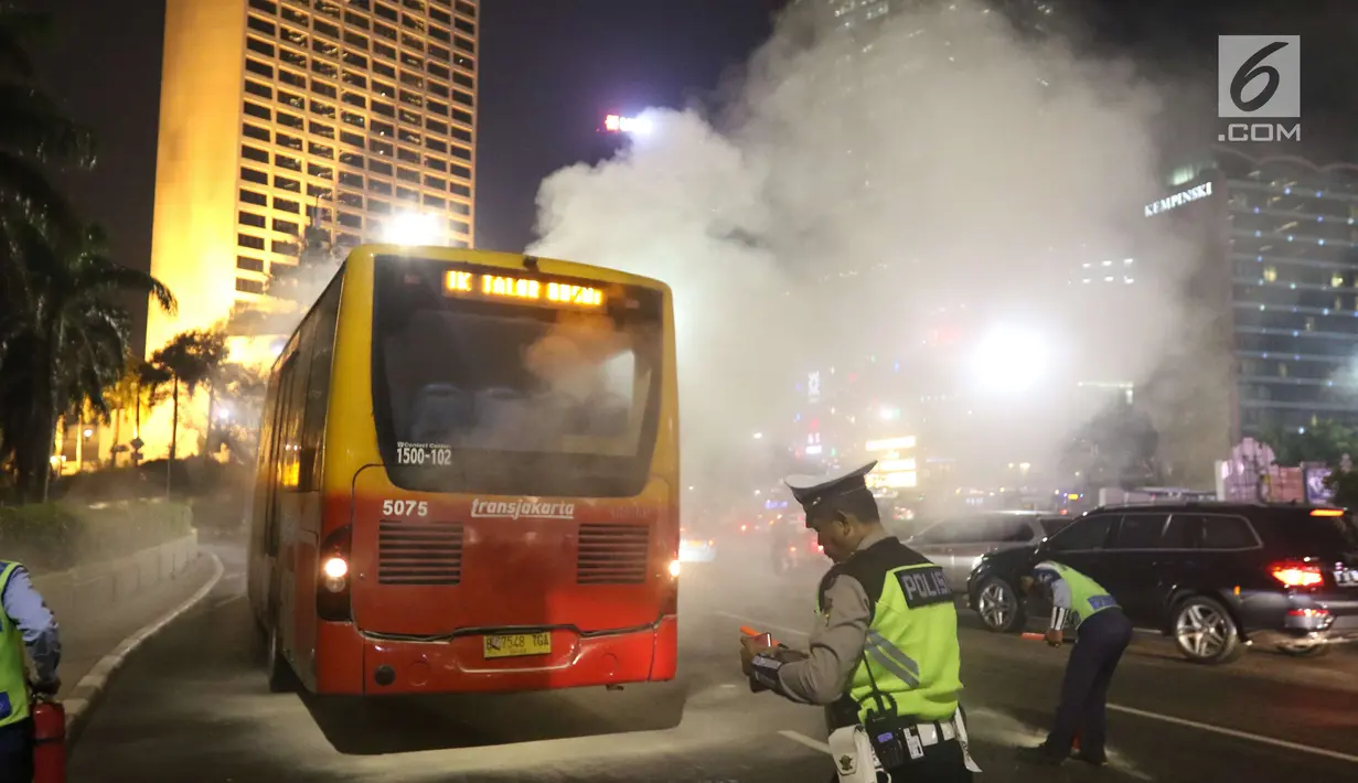 Polisi berjaga di dekat TransJakarta yang mengeluarkan asap dari dalam mobil di Bundaran HI, Jakarta, Rabu (25/4) malam. Belum diketahui penyebab insiden tersebut. (Liputan6.com/Angga Yuniar)
