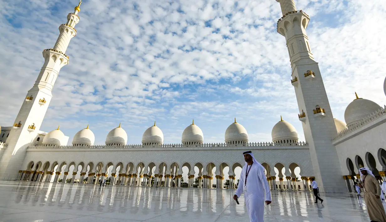 Seorang pria berjalan melewati halaman Masjid Agung Sheikh Zayed di Abu Dhabi, Uni Emirat Arab. Masjid ini adalah masjid terbesar ketiga di dunia setelah masjid di Mekkah dan Madinnah. (Photo by Vincenzo PINTO / AFP)