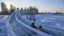 Orang-orang meluncur di seluncuran es di sebuah taman hiburan menjelang Festival Es dan Salju Internasional Harbin Tiongkok ke-39 di Harbin, di provinsi Heilongjiang timur laut China (4/1/2023). (AFP/Hector Retamal)