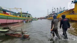 Nelayan melintasi banjir rob saat cuaca ekstrem di Pelabuhan Muara Baru, Penjaringan, Jakarta Utara, Rabu (28/12/2022). Banjir ROB, hujan deras dan  cuaca buruk melanda kawasan Pelabuhan Muara Baru saat siang menjelang sore hari. (Liputan6.com/Johan Tallo)