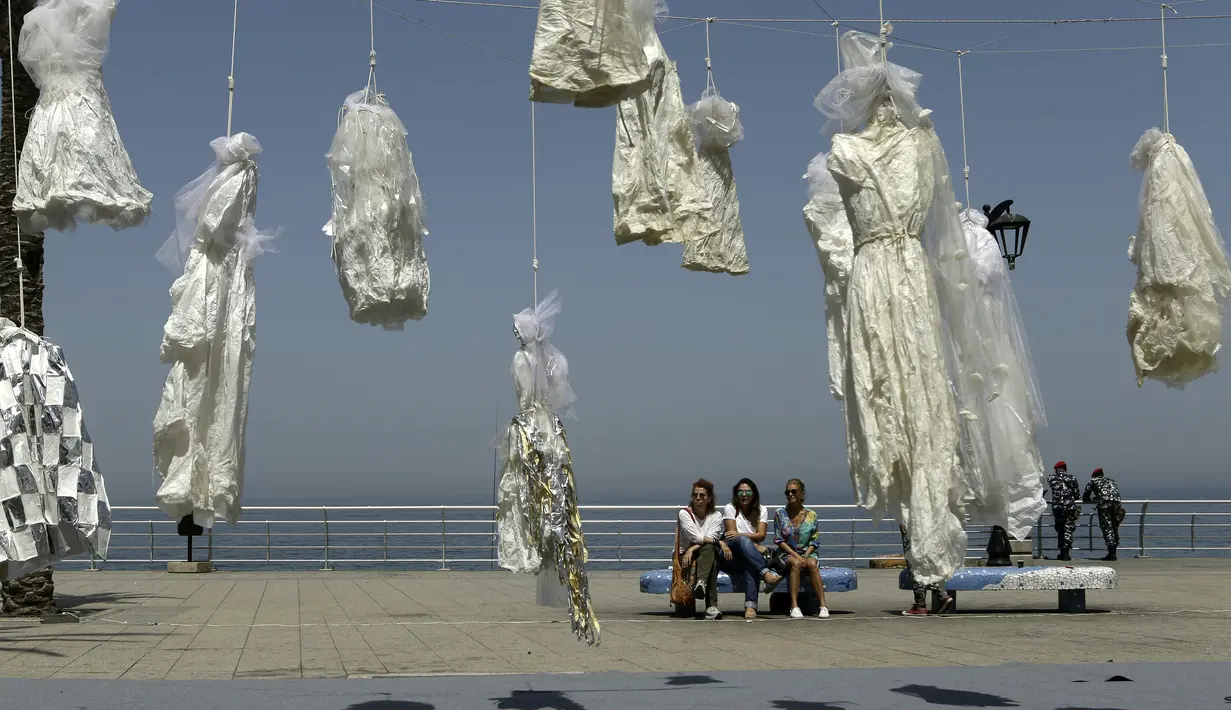 Sejumlah wanita duduk dekat puluhan gaun pengantin yang digantung di tepi pantai Beirut, Sabtu (22/4). Sekitar 30 gaun pengantin menggambarkan kondisi mencekam, lusuh dan berwarna pudar sebagai bentuk protes UU Pemerkosaan di Lebanon. (PATRICK BAZ/AFP)