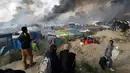 Para imigran melihat tempat penampungan darurat yang terbakar di kamp pengungsian "Jungle" di Calais, Prancis, (26/10). Pengosongan kamp ini sempat mendapat penolakan dari beberapa imigran. (REUTERS/Philippe Wojazer)