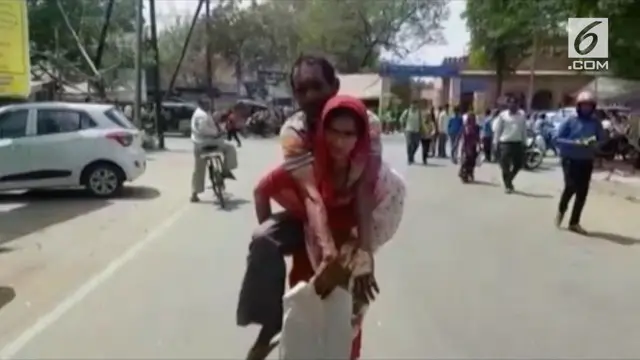 Seorang istri rela menggendong suaminya dan berjalan jauh untuk mendapatkan sebuah kursi roda.
