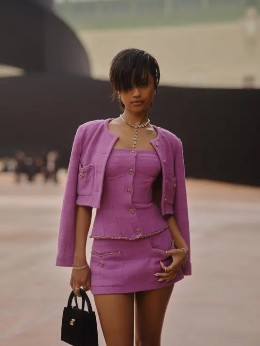 Tyla pilih kenakan strapless dan rok mini tweed berwarna ungu. Cropped jacket berkantung warna senada melapisi outfit minimalisnya. Sebagai aksesori, Tyla kenakan kalung dan tas Chanel hitam [Chanel]