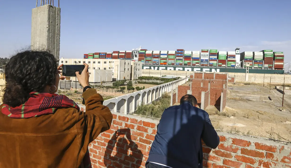 Warga menyaksikan kapal kargo Ever Given usai dibebaskan oleh tim penyelamat setelah terjebak dan memblokir lalu lintas di Terusan Suez, Mesir, Senin (29/3/2021). Kapal keruk dibawa masuk dan menggali 30.000 meter kubik lumpur dan pasir dari bawah ujung kapal. (AP Photo/Mohamed Elshahed)