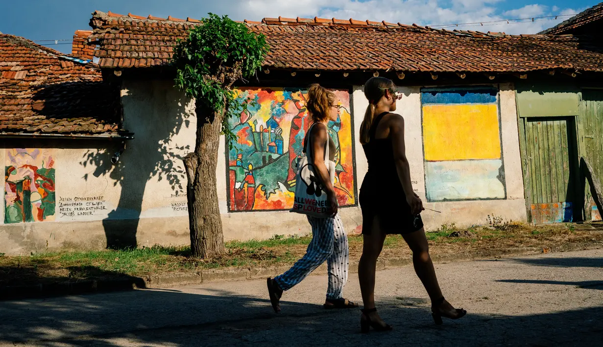 Dua orang wanita melewati lukisan mural karya seniman terkenal di dinding rumah desa Staro Zhelezare di Bulgaria, 4 Agustus 2018. Dengan populasi penduduk dibawah 500 orang, desa ini disulap menjadi galeri seni yang penuh mural. (AFP/Dimitar DILKOFF)