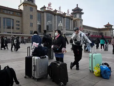 Penumpang membawa tas menunggu kereta di luar pintu masuk stasiun kereta api Beijing di ibu kota China (7/1/2023). Ketika migrasi tahunan dimulai dengan orang-orang yang kembali ke kampung halaman mereka untuk perayaan Tahun Baru Imlek. (AFP/Wang Zhao)