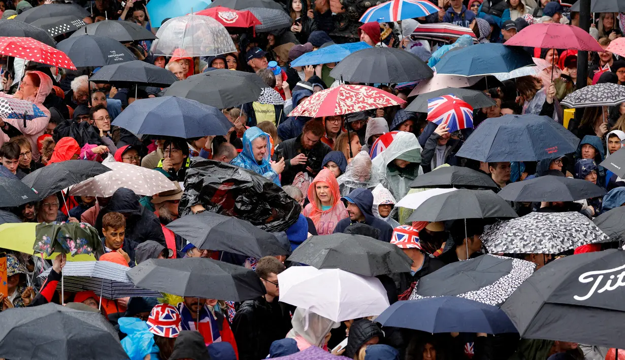 Para simpatisan berteduh dari hujan di bawah payung yang berjejer di sepanjang rute 'Prosesi Raja', yang membentang sejauh dua kilometer dari Istana Buckingham ke Westminster Abbey, sambil menunggu Raja Charles III dan Permaisuri Camilla, melintasi Diamond State Coach, di pusat kota London, Sabtu (6/5/2023). (Photo by PIROSCHKA VAN DE WOUW / POOL / AFP)