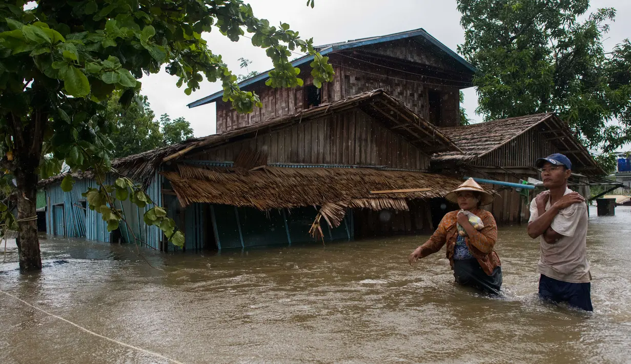 Dua warga melintasi banjir yang merendam di kecamatan Mawlamyine, negara bagian Mon, Myanmar (18/6). Hujan deras mengakibatkan banjir rendam rumah warga dan tanah longsor. (AFP PHOTO / Ye Aung Thu)