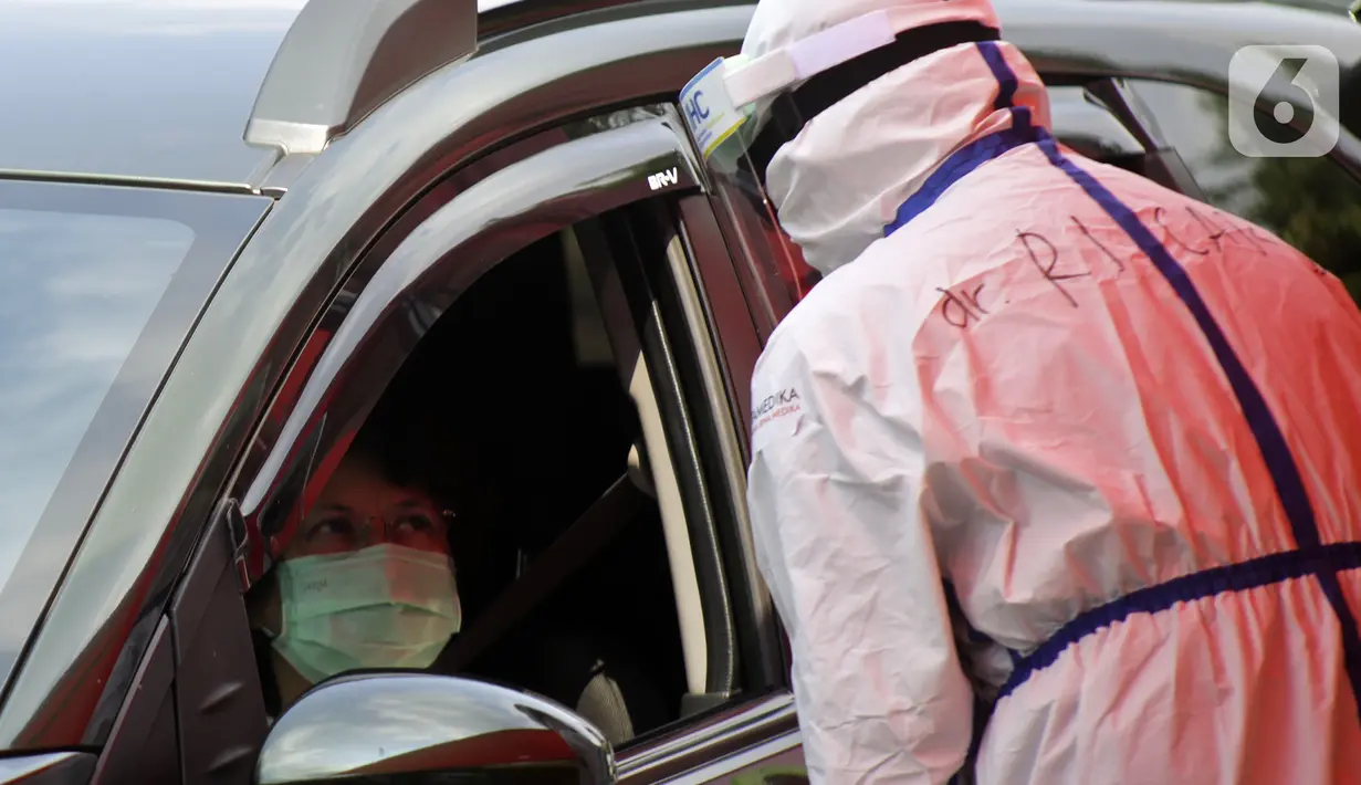 Petugas berpakaian APD lengkap melayani pasien yang secara mandiri melakukan swab test drive thru di halaman parkir rumah sakit di Jakarta, Rabu (12/5/2020). Swab test drive thru dilakukan untuk mendeteksi dan mencegah penyebaran virus corona COVID-19. (Liputan6.com/Johan Tallo)