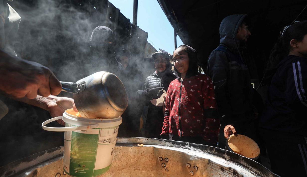 Anak-anak pengungsi Palestina menerima makanan dari dapur amal di kamp pengungsi Nuseirat, Jalur Gaza Tengah pada 13 April 2026. Krisis pangan di Jalur Gaza memasuki fase yang kian mengkhawatirkan. (Eyad Baba/AFP)