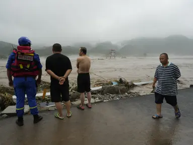 Seorang pekerja penyelamat dan warga lainnya melihat ke arah sungai yang meluap di daerah Miaofengshan di pinggiran Beijing, Selasa, 1 Agustus 2023. (AP Photo/Ng Han Guan)