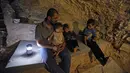 Warga Suriah, Hadheefa al-Shahadh duduk bersama anak-anaknya di dalam gua yang dia gali dalam rumahnya di Desa Maud Shurin, Provinsi Idlib, Selasa (11/). Gua itu dibuat untuk berlindung ketika pemerintah Suriah melakukan serangan. (OMAR HAJ KADOUR/AFP)