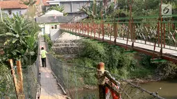 Warga berjalan di samping jembatan gantung yang diberi julukan Indiana Jones di Srengseng Sawah, Jagakarsa, Jakarta, Jumat (3/8). Pemprov DKI membangun jembatan Indiana Jones karena yang lama sudah tidak layak. (Liputan6.com/Immanuel Antonius)