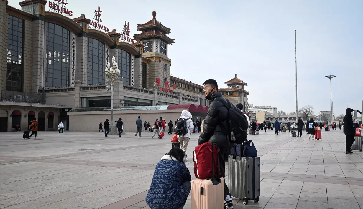 Sepasang suami istri membawa tas menunggu kereta di luar pintu masuk stasiun kereta api Beijing di ibu kota China (7/1/2023). Ketika migrasi tahunan dimulai dengan orang-orang yang kembali ke kampung halaman mereka untuk perayaan Tahun Baru Imlek. (AFP/Wang Zhao)