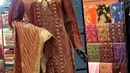 Terbuat dari kain songket bernuansa coklat tembaga dengan detail motif tenun tradisional yang elegan. Atasannya berupa tunik panjang dengan hiasan bordir halus di bagian depan dan tepi lengan, dipadukan dengan bawahan kain songket senada bermotif geometris khas. Set ini dilengkapi selendang songket dengan motif garis vertikal dan aksen floral berwarna emas kehijauan di tepinya. Tampilan semakin mewah berkat aksesori kalung emas besar yang menambah sentuhan tradisional sekaligus anggun. (Foto: instagram@/zainalsongket)