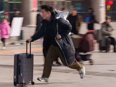 Seorang pria berlari sambil menyeret koper di stasiun kereta api saat orang-orang pulang kampung selama liburan Tahun Baru Imlek di Beijing, China, Selasa 10 Februari 2026. Gelombang migrasi penduduk tahunan terbesar China telah dimulai. (AP Photo/Vincent Thian)