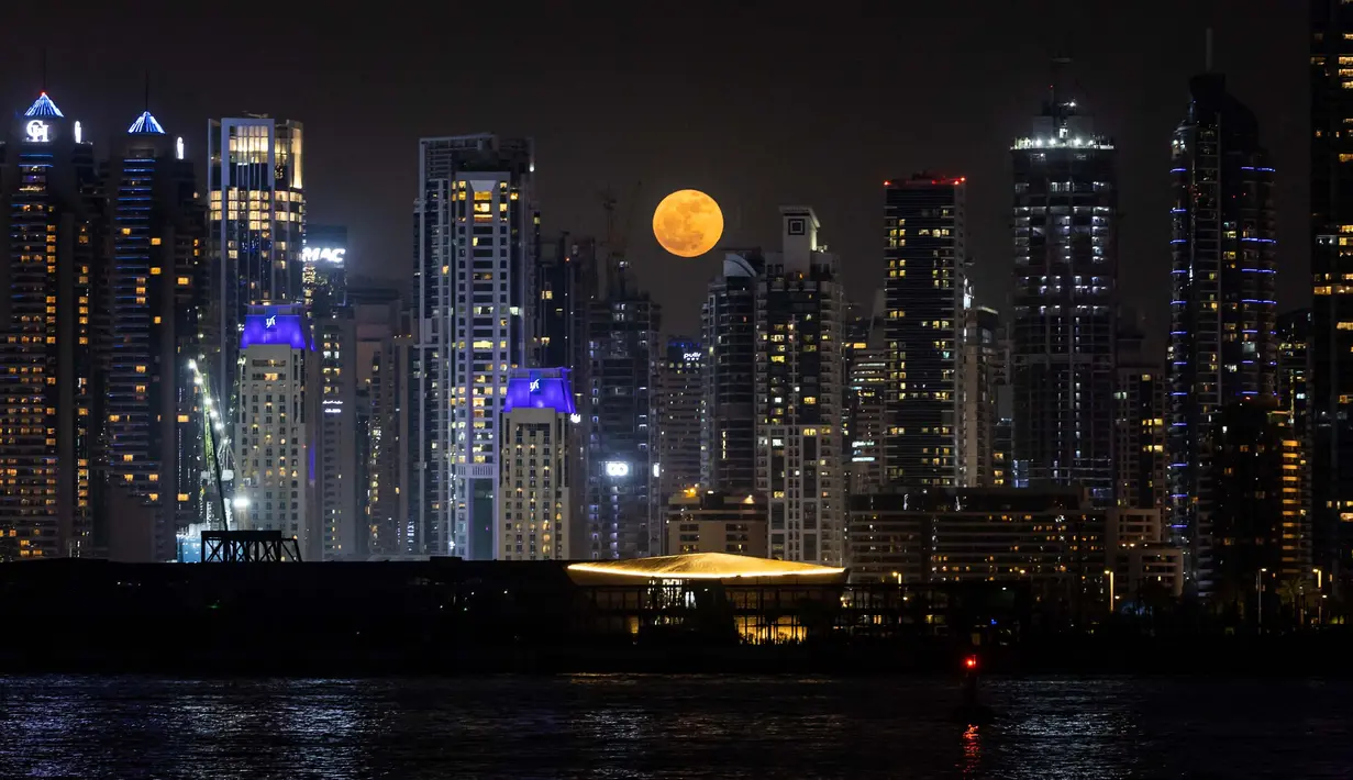 Fenomena Bulan Stroberi bukan hanya suguhan visual, tetapi juga simbol spiritual dan emosional. Tampak dalam foto, bulan purnama yang dikenal sebagai 'Bulan Stroberi' muncul di atas cakrawala Dubai, Uni Emirat Arab pada 11 Juni 2025. (FADEL SENNA/AFP)