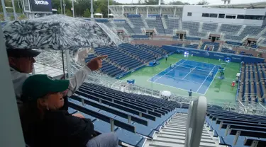 Penonton duduk menunggu penundaan pertandingan akibat hujan selama putaran pertama turnamen tenis AS Terbuka 2017 di Grandstand Stadium, New York (29/8). Meski hujan, para penonton tetap antusias. (AP Photo / Andres Kudacki)