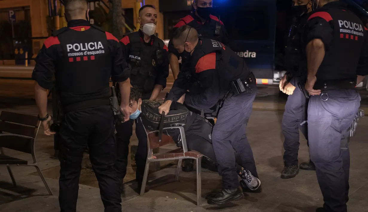 Seorang pemuda ditahan oleh Mossos d'Escuadra, kepolisian regional Catalonia, setelah jam malam di Barcelona pada 1 November 2020. Pemerintah Spanyol menetapkan pembatasan gerak atau jam malam yang berlaku pukul 22.00 untuk mengendalikan lonjakan kasus Covid-19. (AP Photo/Emilio Morenatti)