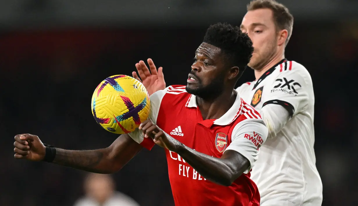 Gelandang Arsenal, Thomas Partey berebut bola dengan gelandang Manchester United, Christian Eriksen dalam laga Liga Inggris 2022/2023 di Emirates Stadium, London (22/1/2023). Thomas Partey yang didatangkan Arsenal pada awal musim 2020/2021 dari Atletico Mdardrid dan masih menjadi andalan Mikel Arteta di lini tengah The Gunners ini tercatat sebagai pemain tertua ketiga dalam skuad Arsenal pada musim 2022/2023 dengan usia 29 tahun. (AFP/Glyn Kirk)