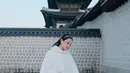 Ia nampak kenakan hanbok dress putih bermotif emas dilapisi coat berbulu warna putih [@alyssadaguise]