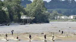 Suasana di Sungai Dordogne, Saint-Pardon, Prancis (24/7). Fenomena pasang surut besar yang menyebabkan gelombang arus di Sungai Dordogne ini dimanfaatkan warga dan turis unutk berselancar. (AFP Photo/Georges Gobet)