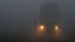 Seorang pria berdiri di samping truk di sepanjang jalan di tengah cuaca berkabut di Lahore (21/12/2022). Beberapa penerbangan dialihkan ke bandara lain akibat cuaca berkabut. (AFP/Arif Ali)