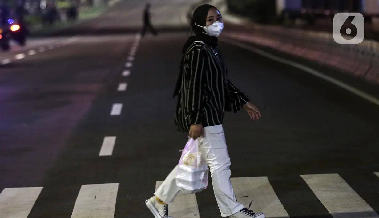 Seorang wanita menyeberang jalan saat berlangsungnya Crowd Free Night di kawasan Bundaran HI, Jakarta, Jumat (31/12/2021). Polda Metro Jaya memberlakukan pengendalian mobilitas Crowd Free Night pada malam Tahun Baru 2022 yang berlangsung mulai pukul 22.00-04.00 WIB. (Liputan6.com/Johan Tallo)