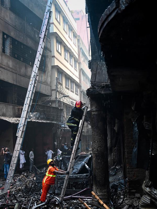 Petugas pemadam kebakaran menggunakan tangga berusaha menaiki gedung apartemen setelah kebakaran di Dhaka (21/2). Setidaknya 69 orang tewas dalam kebakaran besar tersebut. (AFP Photo/Munir Uz Zaman)