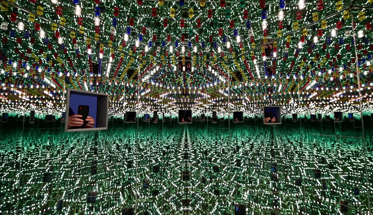 Seorang pengunjung berfoto dengan smartphone-nya di ruang cermin heksagonal berjudul 'Kusama's Peep Show or Endless Love Show' (1966) karya seniman Jepang Yayoi Kusama dalam pameran Yayoi Kusama: A Retrospective di Atrium Martin Gropius Bau, Berlin, Jerman, Selasa (19/5/2021). (John MACDOUGALL/AFP)