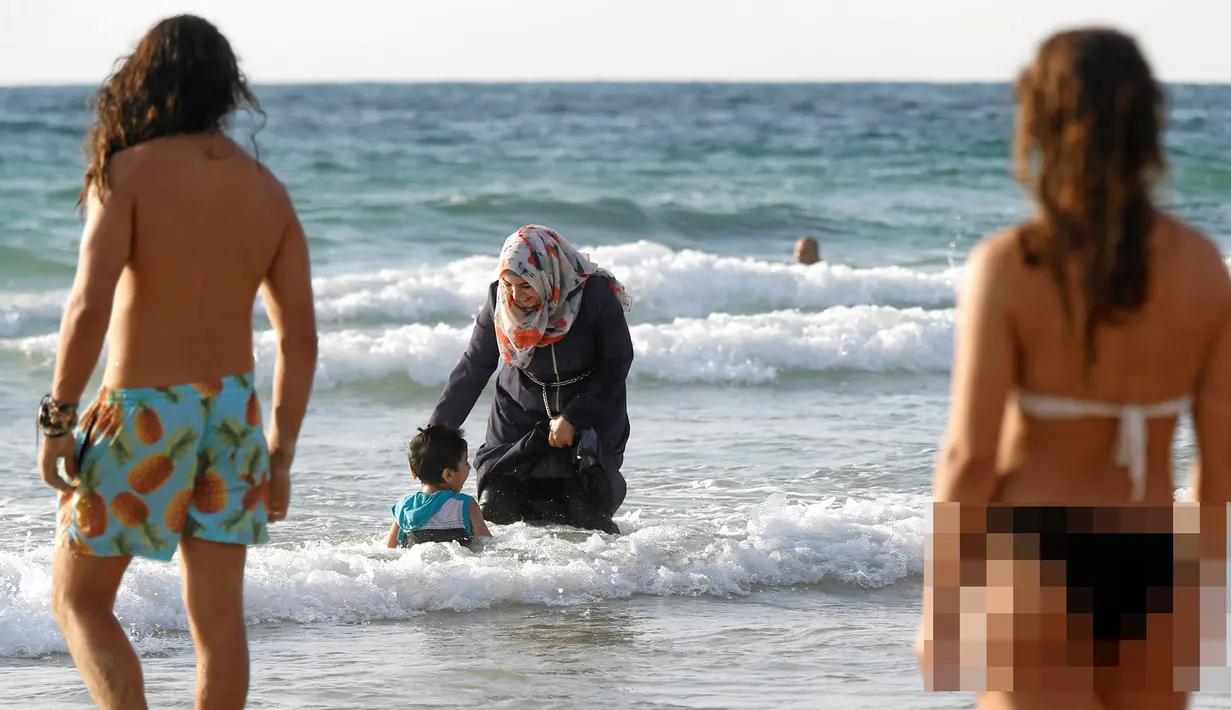 Seorang wanita Muslim bersama anaknya saat berada di pantai di Tel Aviv, Israel pada 22 Agustus 2016. Meski berada di pantai, wanita muslim ini tetap mengenakan jilbab dan busananya. (REUTERS / Baz Ratner)