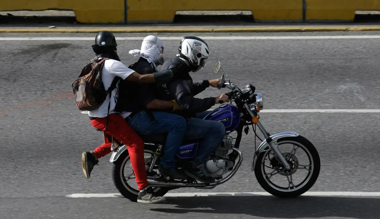Tiga demonstran berada di motor saat terjadi bentrokan dengan pasukan keamanan di Caracas, Venezuela, (31/5). Aksi besar di Venezuela ini merupakan kelanjutan untuk melawan Maduro. (AP Photo/Fernando Llano)