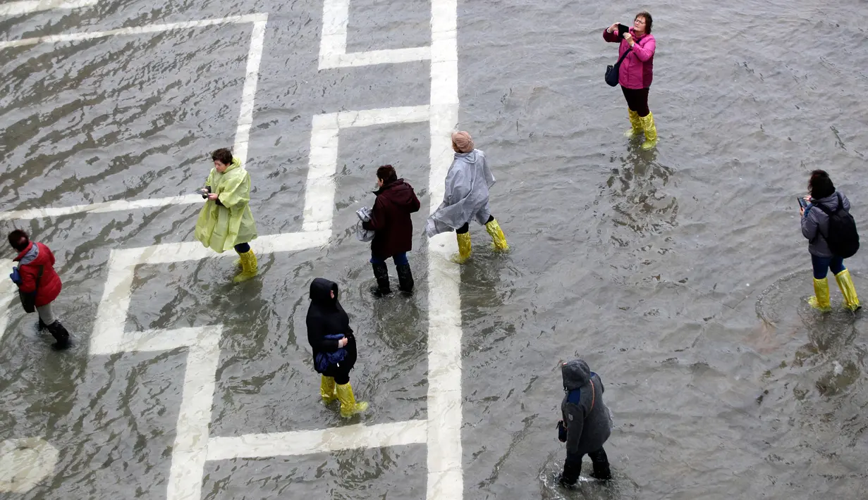 Warga berjalan di Alun-Alun Santo Markus yang banjir akibat terjangan gelombang pasang di Venesia, Italia, Selasa (12/11/2019). Venesia dilanda banjir akibat gelombang pasang setinggi 127 cm. (AP Photo/Luca Bruno)