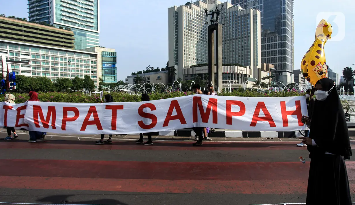 Pengunjung melintas saat warga dari Komunitas Peduli Sampah menggelar aksi saat Hari Bebas Kendaraan Bermotor di Bundaran HI, Jakarta, Minggu (26/6/2022). Kampanye tentang sampah tersebut dalam rangka melanjutkan Pekan Gerakan Jakarta Sadar Sampah yang menghimbau masyarakat untuk saling menjaga kebersihan lingkungan. (Liputan6.com/Johan Tallo)