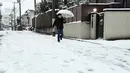 Seorang pria menggunakan payung berjalan di tumpukan salju yang menutupi jalanan di Tokyo, Jepang, Senin (18/1). Akibat banyaknya tumpukan salju yang menyelimuti daerah metropolitan Tokyo, moda transportasi massa pun lumpuh. (AFP PHOTO/Yoshikazu Tsuno)