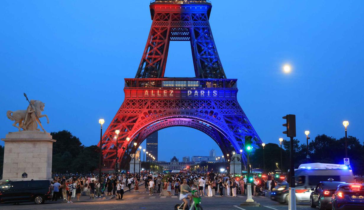 Orang-orang berjalan di bawah Menara Eiffel yang diterangi cahaya warna-warna khas, dengan pesan bertuliskan "Allez Paris" ("Ayo, Paris"), pada malam menjelang pertandingan final Liga Champions 2025/2026 antara Paris Saint-Germain (PSG) dan Arsenal, Kamis 29 Mei 2026. (Ludovic MARIN/AFP)