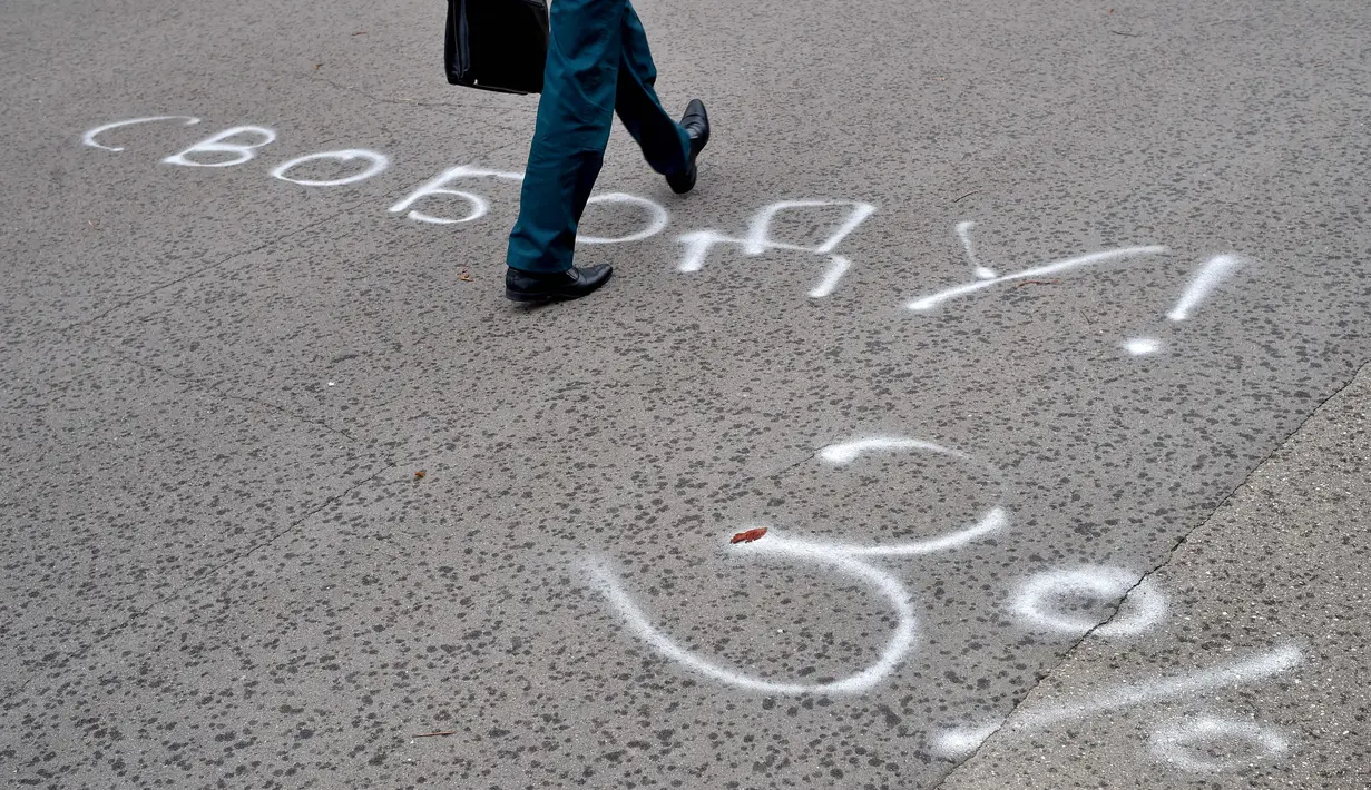 Seorang pria berjalan di halaman aspal yang dilukis dengan tulisan "Kebebasan! 3%", mengacu pada Alexander Lukashenko, yang dijuluki "Sasha 3 persen" dalam ejekan pada peringkat populernya yang seharusnya rendah, di Minsk (25/8/2020). (AFP/Sergei Gapon)