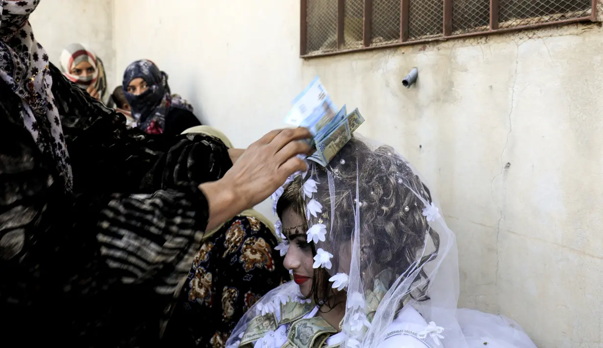 Seorang wanita menaruh uang di kepala pengantin wanita, Heba saat prosesi pernikahan di Raqqa, Suriah (27/10). Heba dan Ahmed merupakan pasangan pertama yang menikah usai Kota Raqqa jatuh dari tangan ISIS. (AFP Photo/Delil Souleiman)