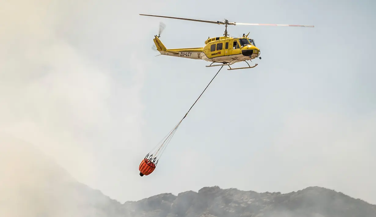 Sebuah helikopter membawa air untuk membantu memadamkan kebakaran yang melanda kawasan Somerset West dekat Cape Town, Afrika Selatan, Rabu (4/1). Kebakaran tersebut telah menghancurkan sebagian wilayah perkebunan tertua di Afsel. (AP Photo / Stefan Smuts)