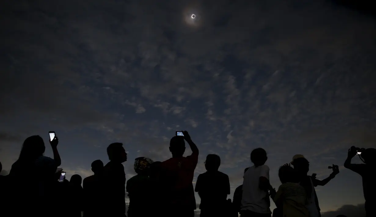 Sejumlah orang melihat dan mengambil gambar dari fenomena Gerhana Matahari Total (GMT) di pantai di pulau Ternate, Indonesia, Rabu (9/3/2015). (REUTERS / Beawiharta)