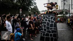 Seorang pria berbaring dan pria lainnya melompat diatasnya saat melakukan lompat batu dalam sebuah acara pagelaran seni dan kebudayaan Nias di Jalan Imam Bonjol, Jakarta, Minggu (12/2). (Liputan6.com/Faizal Fanani)