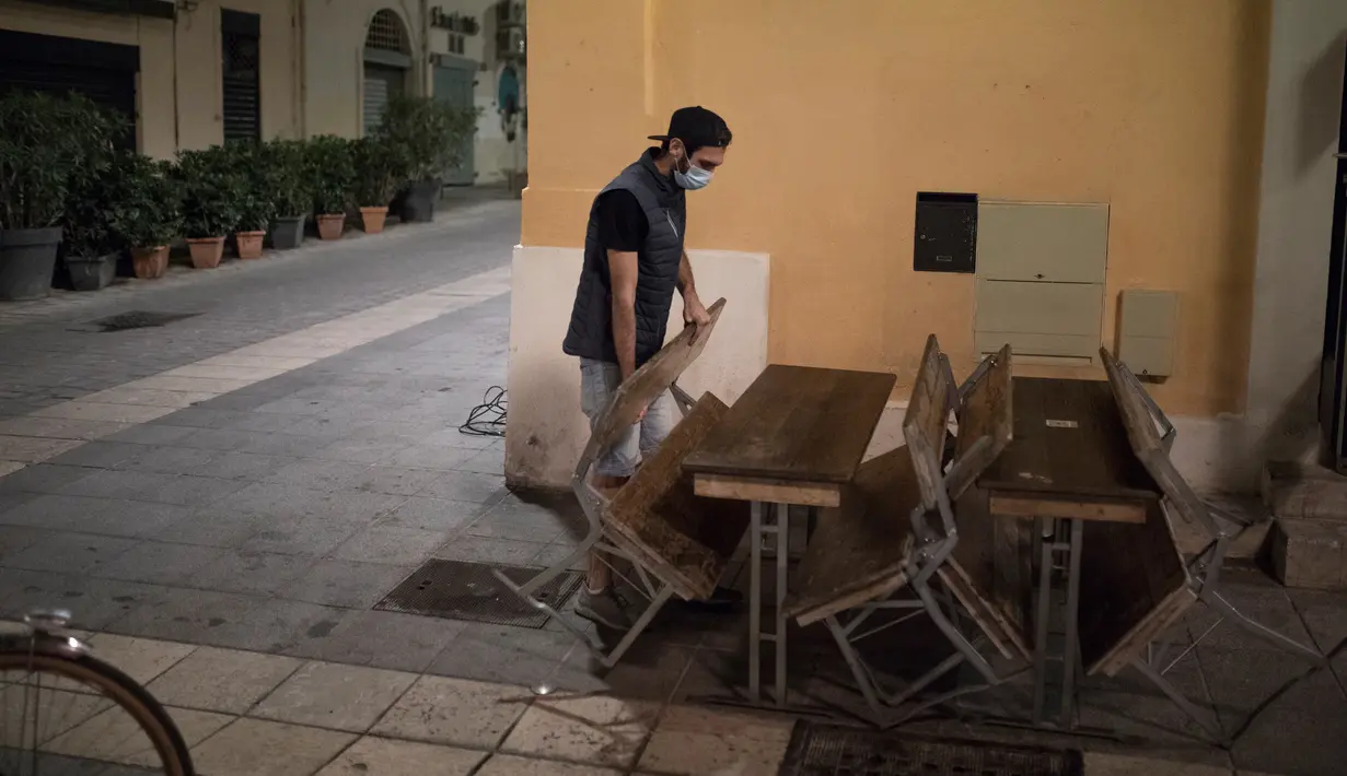 Seorang manajer bar menutup teras barnya di Marseille, selatan Prancis, Minggu (27/9/2020). Restoran dan bar di Marseille pada hari Minggu bersiap tutup selama sepekan sebagai bagian dari pembatasan baru baru Covid-19. (AP Photo/Daniel Cole)