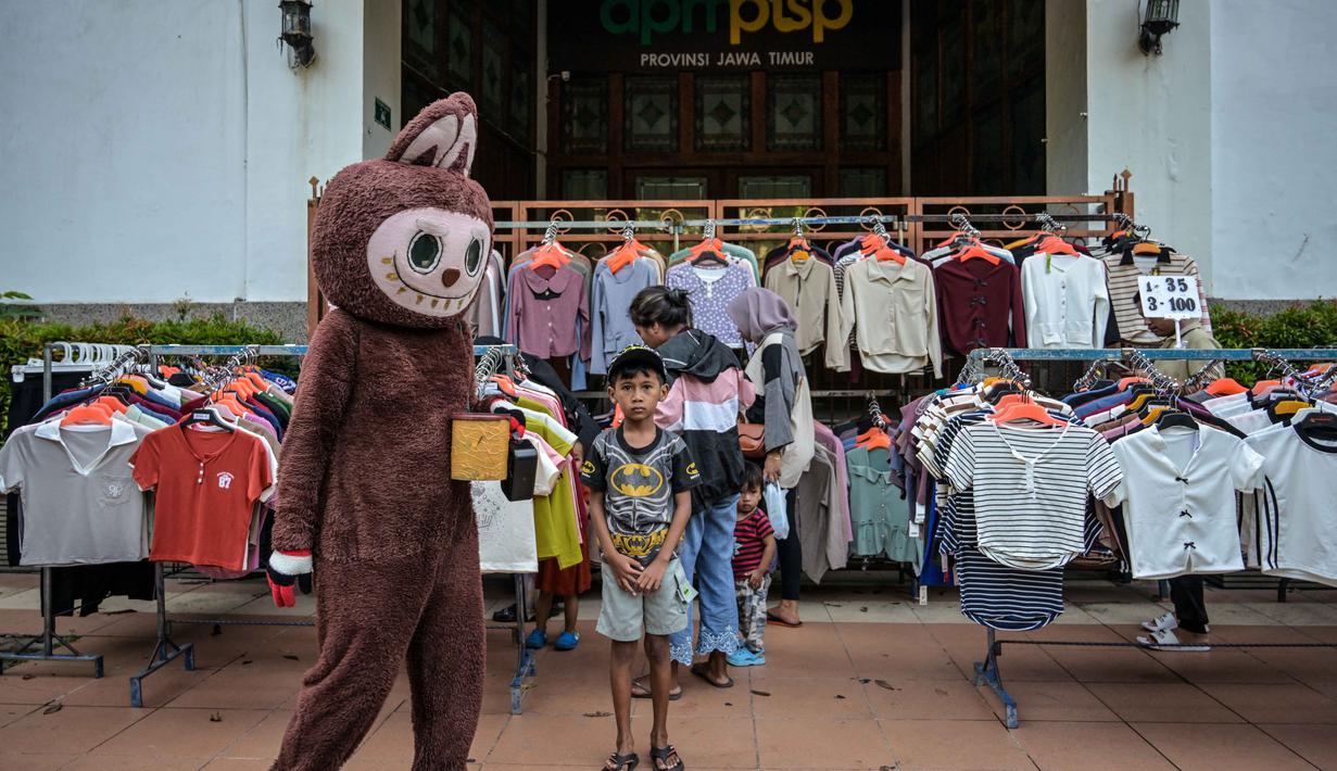 Sensus yang dijadwalkan berlangsung pada 1 Mei hingga 31 Juli 2026, untuk memetakan kondisi riil seluruh pelaku usaha di Indonesia, termasuk usaha mikro kecil menengah (UMKM). Tampak dalam foto, seseorang yang menggunakan kostum berjalan melewati seorang anak laki-laki yang sedang memperhatikan orang-orang berbelanja di kios pakaian di salah satu ruas jalan, Surabaya, Jawa Timur, pada Minggu 19 April 2026. (JUNI KRISWANTO/AFP)