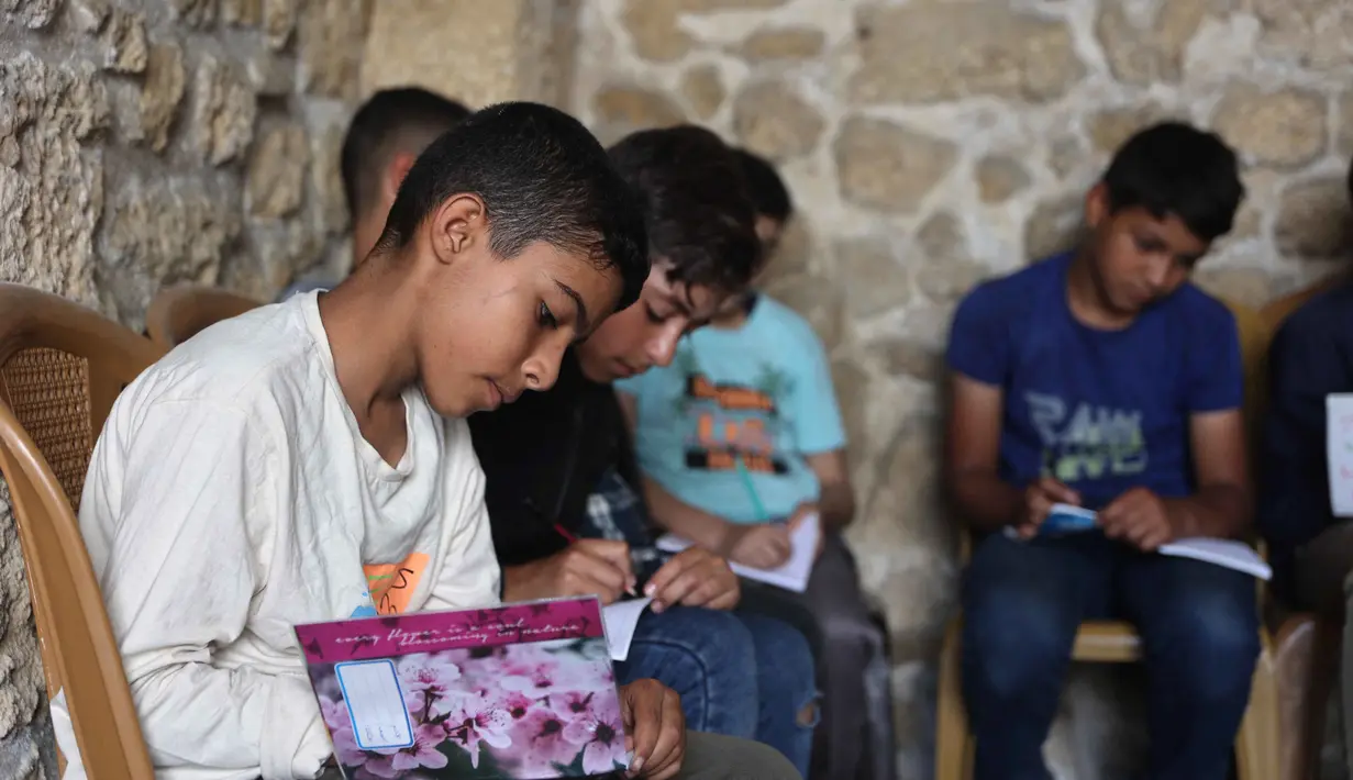 Anak-anak Palestina mencatat saat menghadiri kelas di sekolah bersejarah "Al-Kamaliya al-Othmanya" di Kota Tua Gaza yang menjadi bagian dari inisiatif sukarelawan yang diorganisir oleh para guru pengungsi, di Kota Gaza pada 2 November 2025. Saat ini, diperkirakan sekitar satu dari enam anak usia sekolah telah kembali ke kelas untuk kembali mengikuti kegiatan belajar.  (Omar AL-QATTAA/AFP)