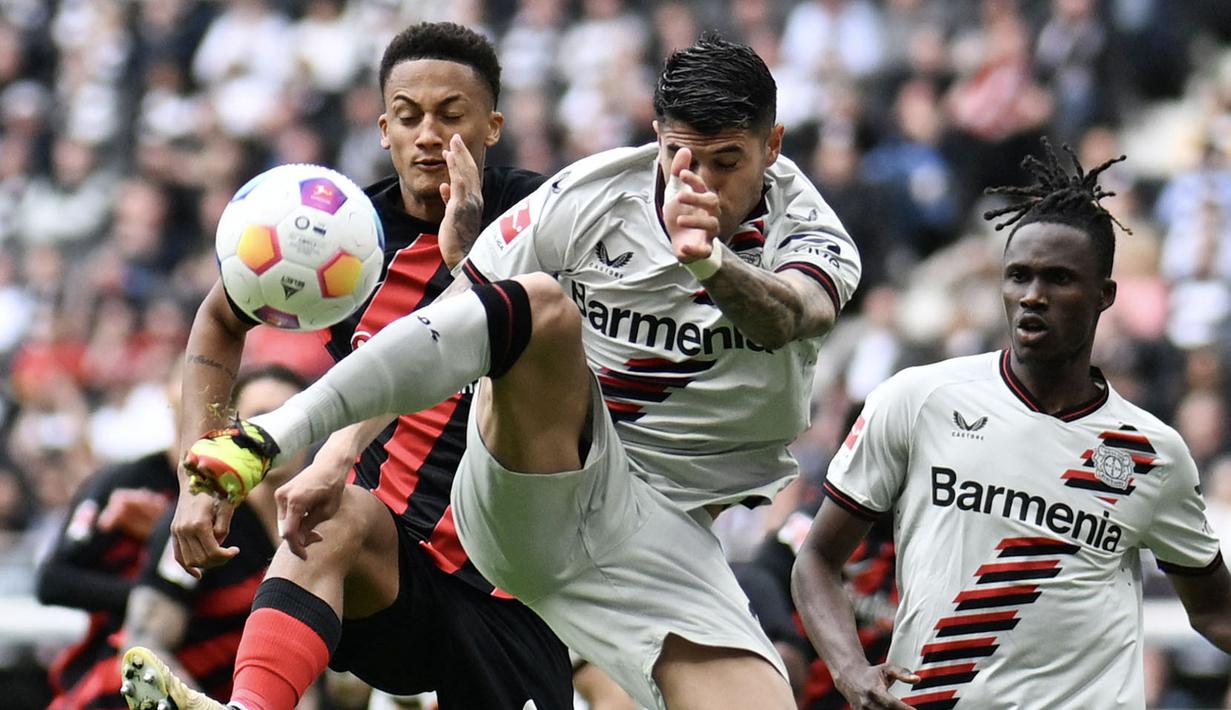Pemain Bayer Leverkusen, Josip Stanisic, berebut bola dengan pemain Eintracht Frankfurt, Tuta pada laga Liga Jerman di Stadion Deutsche Bank Park, Senin (6/5/2024). Kemenangan ini memperpanjang rekor tidak terkalahkan mereka pada musim ini menjadi 48 laga. (AFP/Kirill Kudryavsev)